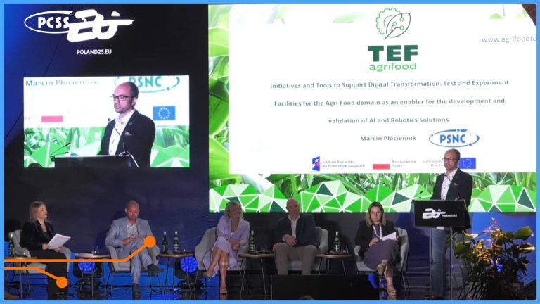 Zdjęcie przedstawia panel dyskusyjny lub prezentację podczas wydarzenia związanego z technologią i rolnictwem. Na dużym ekranie w tle widnieje logo "TEF agrifood" oraz tytuł "Initiatives and Tools to Support Digital Transformation. Test and Experiment Facilities for the Agri-Food domain as an enabler for the development and validation of AI and Robotics Solutions", co wskazuje na tematykę spotkania. Widoczny jest również napis "Marcin Płóciennik" i logo "PCSS" (Poznańskie Centrum Superkomputerowo-Sieciowe), sugerując, że jest to jeden z prelegentów lub instytucji zaangażowanych w projekt. Na scenie siedzi pięć osób, a po prawej stronie, za mównicą, stoi wspomniany Marcin Płóciennik – kierownik Działu Technologii Internetu Rzeczy PCSS.