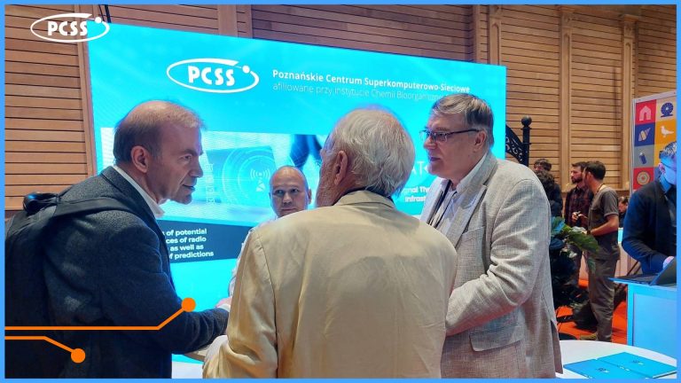 Obrazek przedstawia grupę osób stojących i rozmawiających na stoisku wystawienniczym. W tle widoczny jest duży, podświetlany ekran z logo "PCSS" i napisem "Poznańskie Centrum Superkomputerowo-Sieciowe" oraz tekstem częściowo zasłoniętym przez osoby. Trzy osoby w centrum są pochylone ku sobie, angażując się w ożywioną dyskusję. W tle po prawej stronie widać fragmenty innych stoisk i więcej osób.