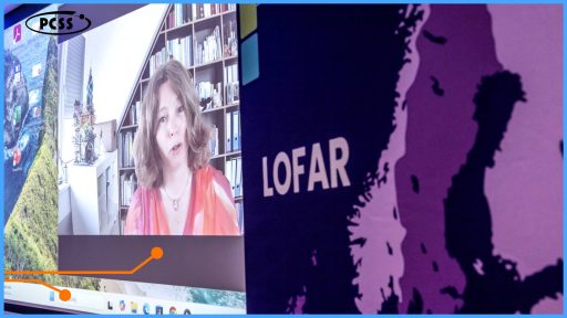 Na grafice widoczne są dwa główne ekrany. Na lewym ekranie wyświetlana jest wideokonferencja z kobietą, która mówi. W tle za nią znajduje się regał z książkami. Prawy ekran przedstawia duży napis "LOFAR" oraz mapę lub kontur lądowy w odcieniach fioletu. W dolnej części lewego ekranu widoczne są fragmenty paska zadań systemu operacyjnego oraz pomarańczowa, zakrzywiona linia graficzna.