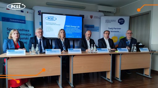 Na grafice widoczne jest spotkanie panelowe, w którym uczestniczy sześć osób siedzących za stołami, zwróconych przodem do widza. Za panelistami znajduje się duży ekran prezentujący logo PCSS Energy Lab oraz inne informacje. Po lewej stronie ekranu widać logo Unii Europejskiej i napis "Fundusze Europejskie", a po prawej logo Agencji Rozwoju Regionalnego S.A. w Koninie.
