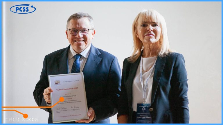 Na środku zdjęcia znajduje się dwoje dorosłych ludzi w formalnych strojach, stojących na tle niebieskiej ściany z logo PCSS. Mężczyzna po lewej, w granatowym garniturze i okularach, uśmiecha się, trzymając w rękach dyplom z napisem "Virtuti Medicinali 2025" przyznany "Dr hab. Cezary MAZUREK". Kobieta po prawej, w czarnym żakiecie, ma na szyi identyfikator z widocznym nazwiskiem "PROF. DR HAB. JOLANTA LOREK-POGORZELSKA".