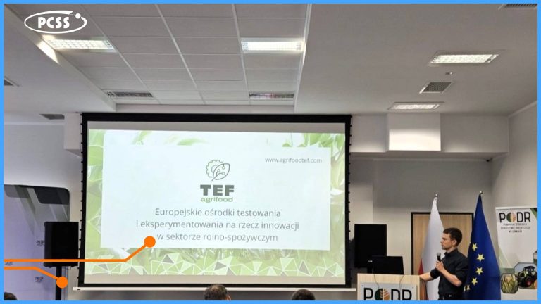 Na zdjęciu widać salę konferencyjną, w której prelegent w czarnej koszulce stoi za mównicą, prezentując slajd na dużym ekranie. Slajd przedstawia logo "TEF agrifood" i tytuł "Europejskie ośrodki testowania i eksperymentowania na rzecz innowacji w sektorze rolno-spożywczym". W tle widać flagi Unii Europejskiej i Polski, a także częściowo widoczne logo PCSS w lewym górnym rogu.