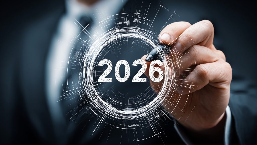 Grafika przedstawia osobę w garniturze, która trzyma pióro skierowane w stronę świecącego, futurystycznego okręgu z wpisanym centralnie rokiem 2026. Całość utrzymana jest w ciemnej, technologicznej stylistyce, symbolizującej planowanie przyszłości lub nowoczesne innowacje.