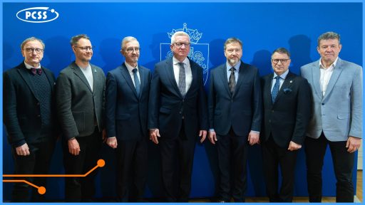 Siedmiu mężczyzn w strojach biznesowych stoi na tle niebieskiej ścianki z logotypem PCSS oraz herbem Poznania. Grupa reprezentuje przedstawicieli nauki, biznesu i samorządu, współpracujących przy rozwoju infrastruktury sztucznej inteligencji. Zdjęcie dokumentuje gotowość Poznania do realizacji projektu Gigafabryki AI.