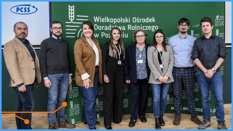 Zdjęcie przedstawia grupę ośmiu osób stojących na tle zielonej ścianki z logotypem Wielkopolskiego Ośrodka Doradztwa Rolniczego w Poznaniu. Uczestnicy spotkania są ubrani w stroje biznesowe i casualowe, a w lewym górnym rogu widoczne jest logo PCSS. Fotografia dokumentuje współpracę lub szkolenie realizowane przez obie instytucje.