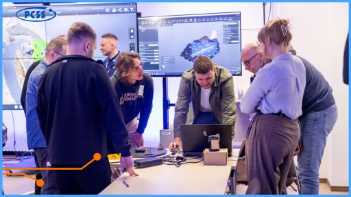 Uczestnicy warsztatów pracują wspólnie przy stanowisku do digitalizacji 3D, obserwując proces skanowania obiektu i analizując model wyświetlany na monitorach w laboratorium PCSS.