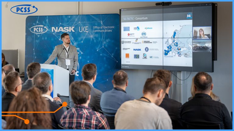 Prelegent w jasnej marynarce przemawia do grupy osób zgromadzonych w sali konferencyjnej, stojąc obok dużego ekranu wyświetlającego mapę Europy i logotypy partnerów. W tle widoczna jest niebieska ścianka z napisami PCSS, NASK oraz UKE. Zdjęcie przedstawia profesjonalne wydarzenie biznesowe lub naukowe dotyczące technologii 5G.