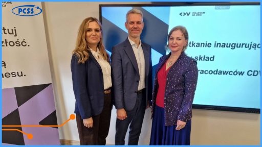 Trzy osoby w strojach biznesowych stoją obok ekranu wyświetlającego informację o spotkaniu inauguracyjnym Rady Pracodawców CDV. Po lewej stronie widoczny jest fragment roll-upu z logiem PCSS. Zdjęcie dokumentuje oficjalne wydarzenie o charakterze zawodowym w jasnym, biurowym wnętrzu.