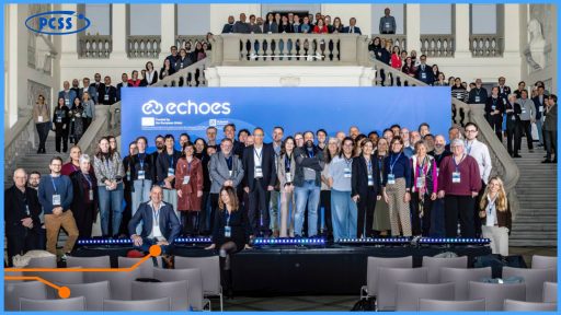 Zdjęcie grupowe kilkudziesięciu uczestników konferencji projektowej ECHOES, pozujących na tle dużej niebieskiej ścianki z logo projektu i Unii Europejskiej. Grupa znajduje się w reprezentacyjnym, klasycznym wnętrzu Muzeum Narodowego w Poznaniu, stojąc na scenie oraz na schodach prowadzących na antresolę. W lewym górnym rogu widoczne jest logo PCSS, a na pierwszym planie puste rzędy krzeseł konferencyjnych.
