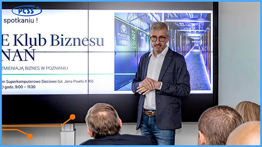 Obrazek przedstawia dyrektora PCSS Roberta Pękala na tle prezentacji w trakcie spotkania Klubu Biznesu. Mężczyzna stoi na tle wyświetlanego na projektorze slajdu, na którym widnieje element serwerowni.